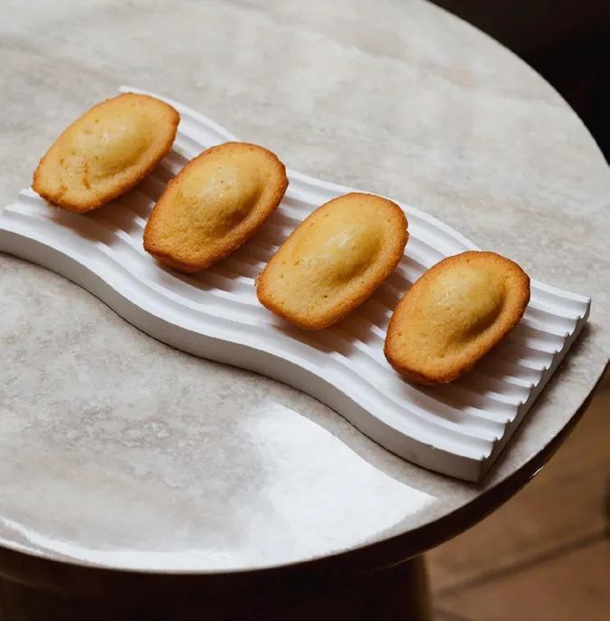 Vier Madeleines auf einer weißen gerillten Schale, Foto von Fauchon